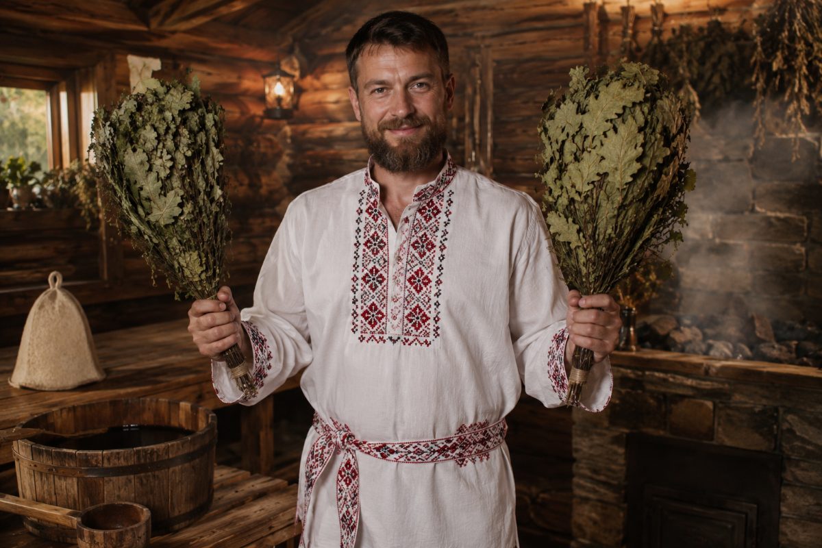 Банщик в льняной рубахе с вышивкой, с дубовыми вениками