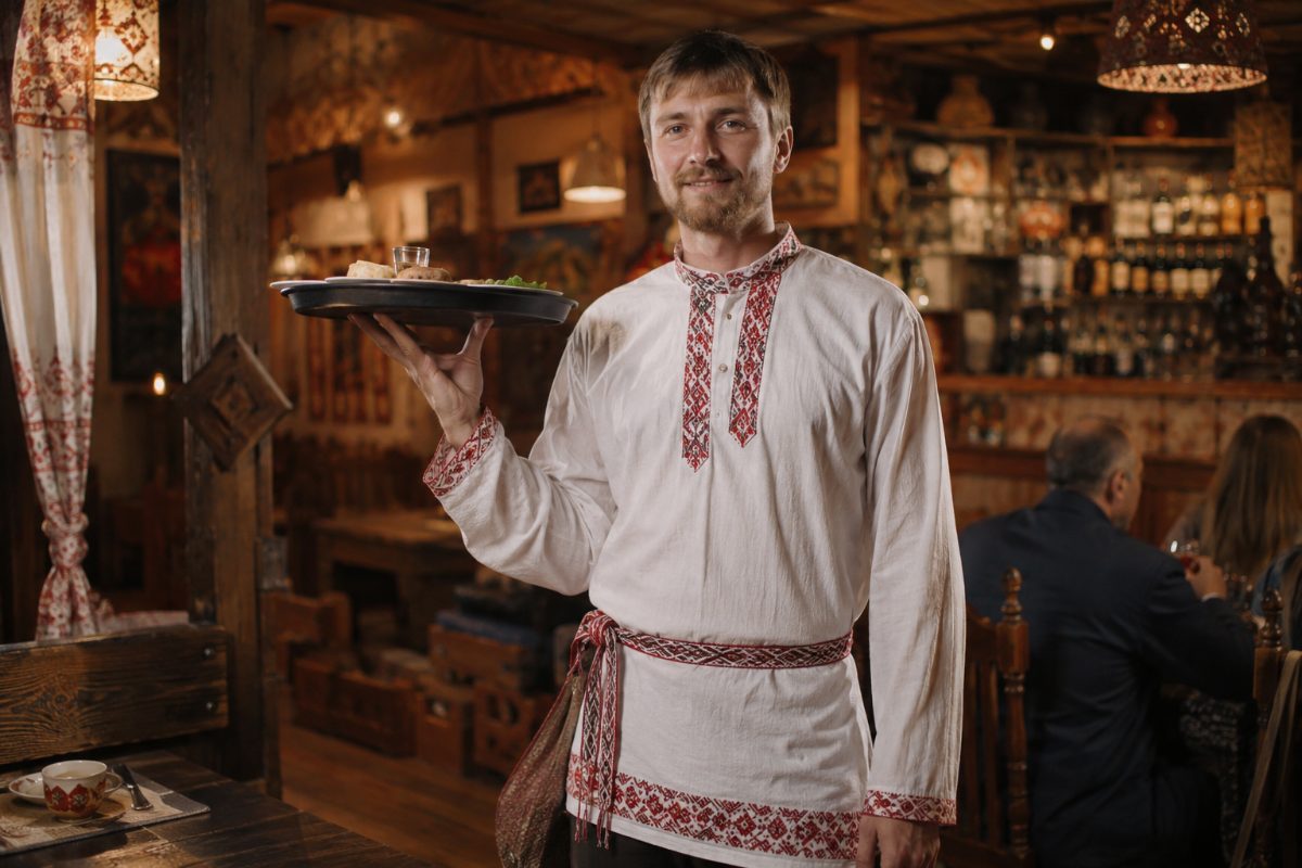 Официант в вышитой косоворотке в ресторане русской кухни